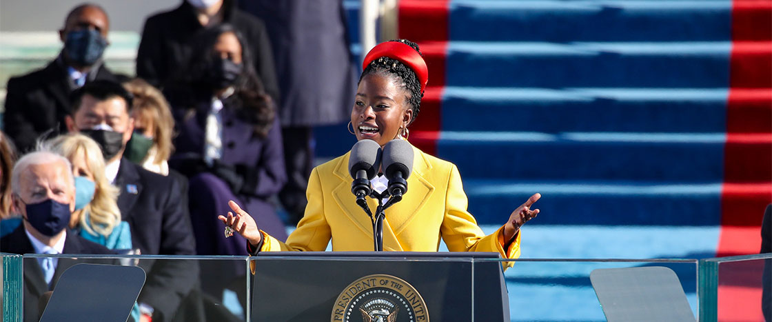 A girl in a yellow jacket passionately receiting a poem to an audience