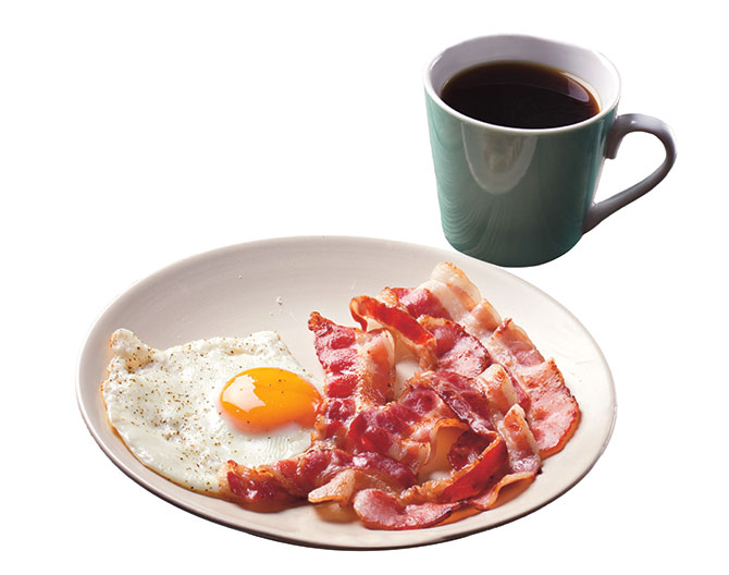 A cup of coffee next to a plate of bacon and an egg