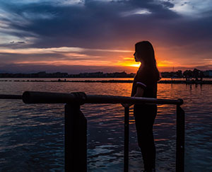 a woman stands in front of a sunset