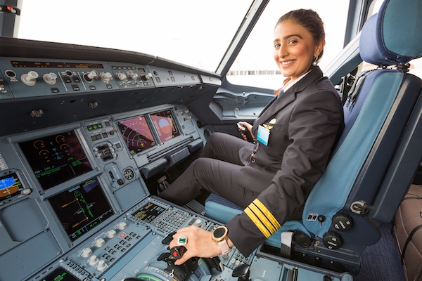 A woman in a pilot&apos;s uniform smiling as she sits in the front seat of a plane cockpit
