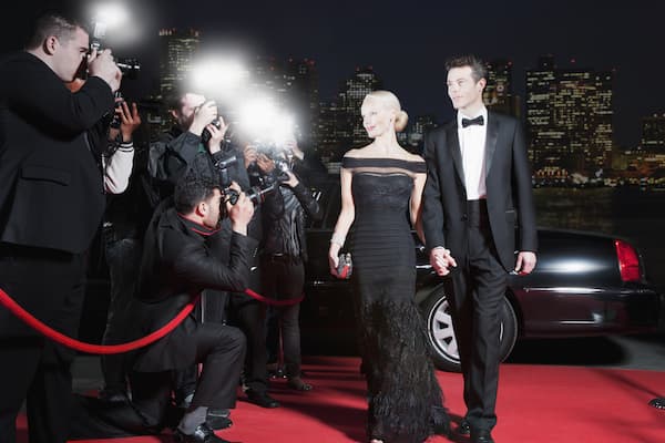 A well dressed couple walking down the red carpet as photographers snap their picture