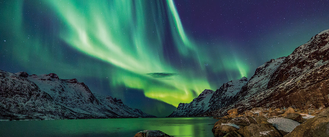 The sky bathed in neon lights with snow covered mountains below it