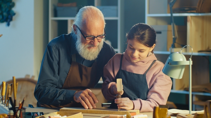 Image of a grandfather helping his granddaughter create an object out of wood