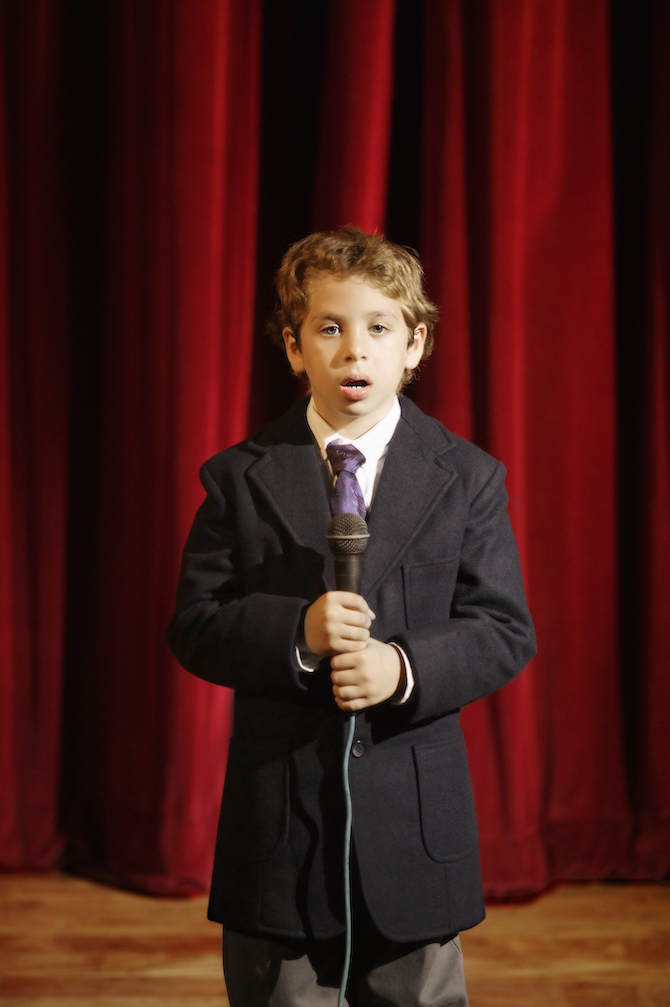 Photo of a boy holding a microphone and staring blankly on stage