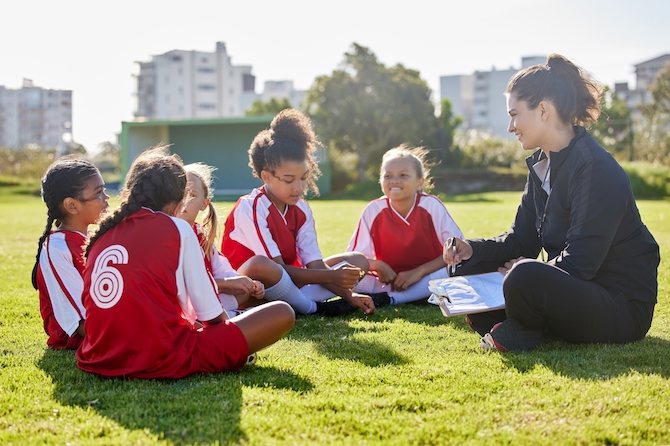 Photo of a coach sitting in a circle with her soccer players