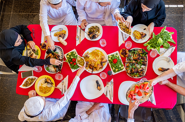 A red table covered from end to end by plates of food as people sit and eat