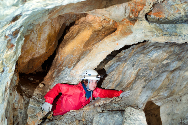 A person wearing a hardhat with a flashlight on it climbing through a cave